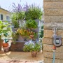 Gardena Bewässerungscomputer Flex am Wasserhahn mit bepflanztem Balkon im Hintergrund.