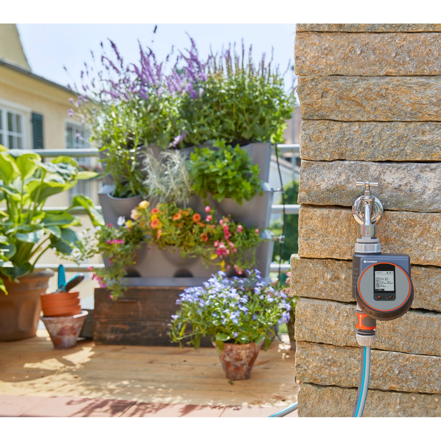 Gardena Bewässerungscomputer Flex am Wasserhahn mit bepflanztem Balkon im Hintergrund.
