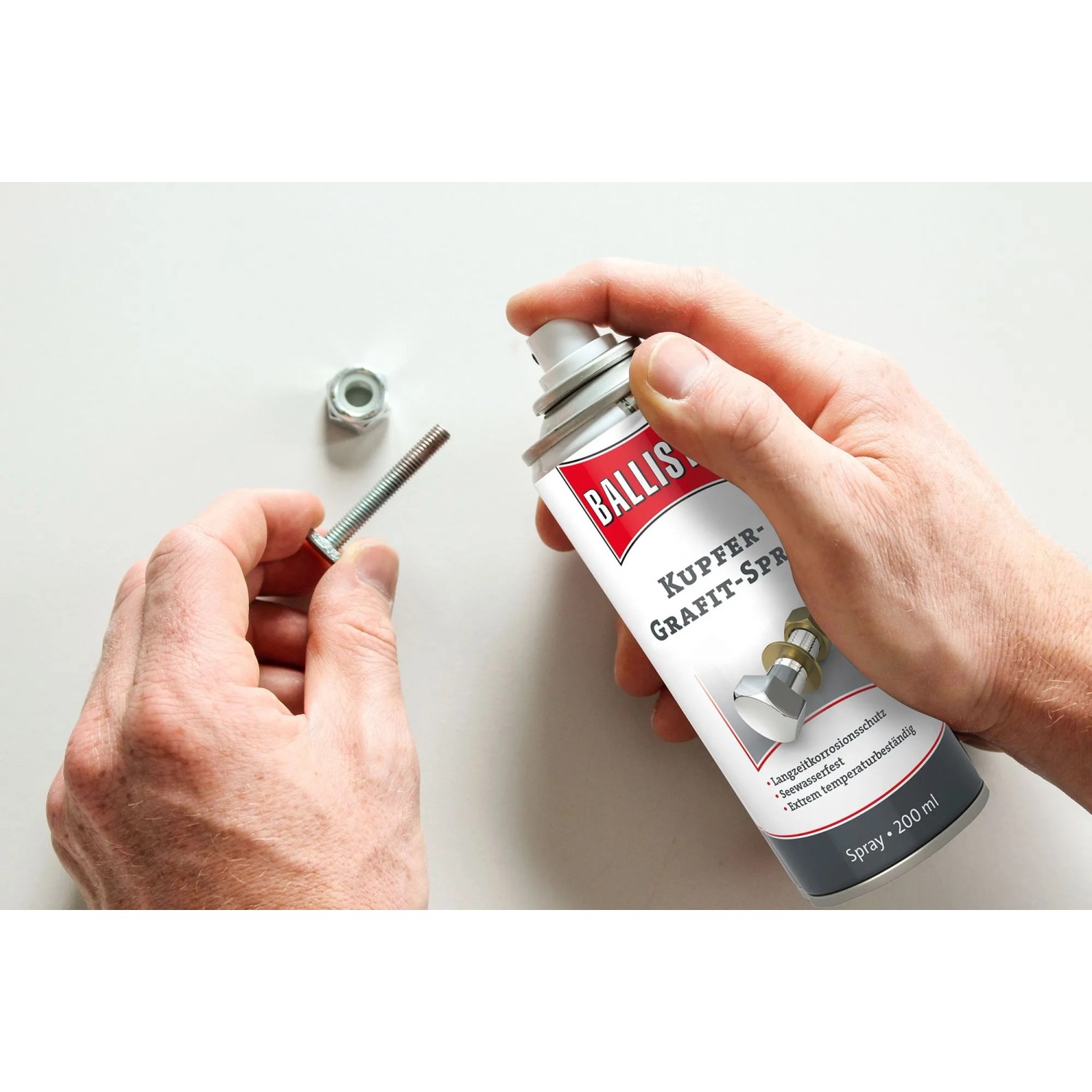 Hand sprüht Ballistol Kupfer-Grafit-Spray auf Schraube und Mutter. Schützt Gewinde vor Festfressen und Korrosion.