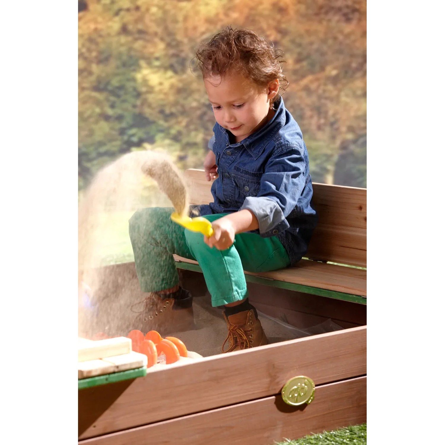 Axi Ella Sandkasten aus Holz, braun-grün, mit Kind beim Spielen im Garten.