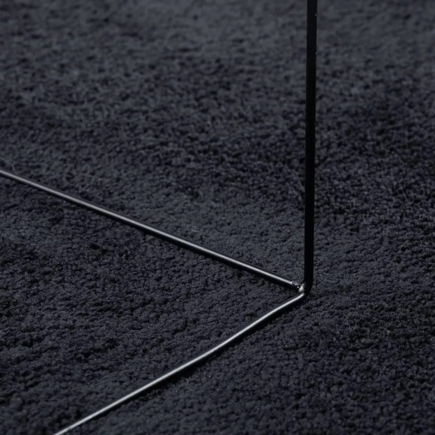 Detailaufnahme: Schwarzer Kurzflor Teppich OVIEDO (200x200 cm) mit Metallgestell.