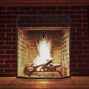 Schwarzes Relaxdays Funkenschutzgitter aus Schmiedeeisen vor Kamin mit Feuer.