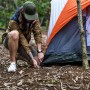 Mann befestigt orange Felsbodenheringe aus verzinktem Stahl am Zelt im Wald. 10er Set Erdanker für Camping & harte Böden.