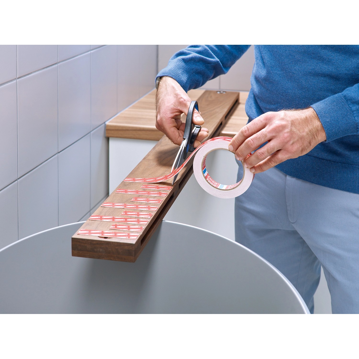 Anwendung Tesa Montageband für Fliesen/Metall: Person schneidet Klebeband mit Schere.