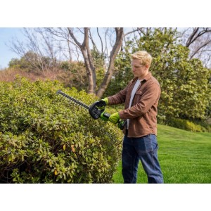 Mann schneidet grüne Hecke mit Greenworks Akku-Heckenschere, 61 cm Klinge. Gartenarbeit, präzise Heckenschnitte.