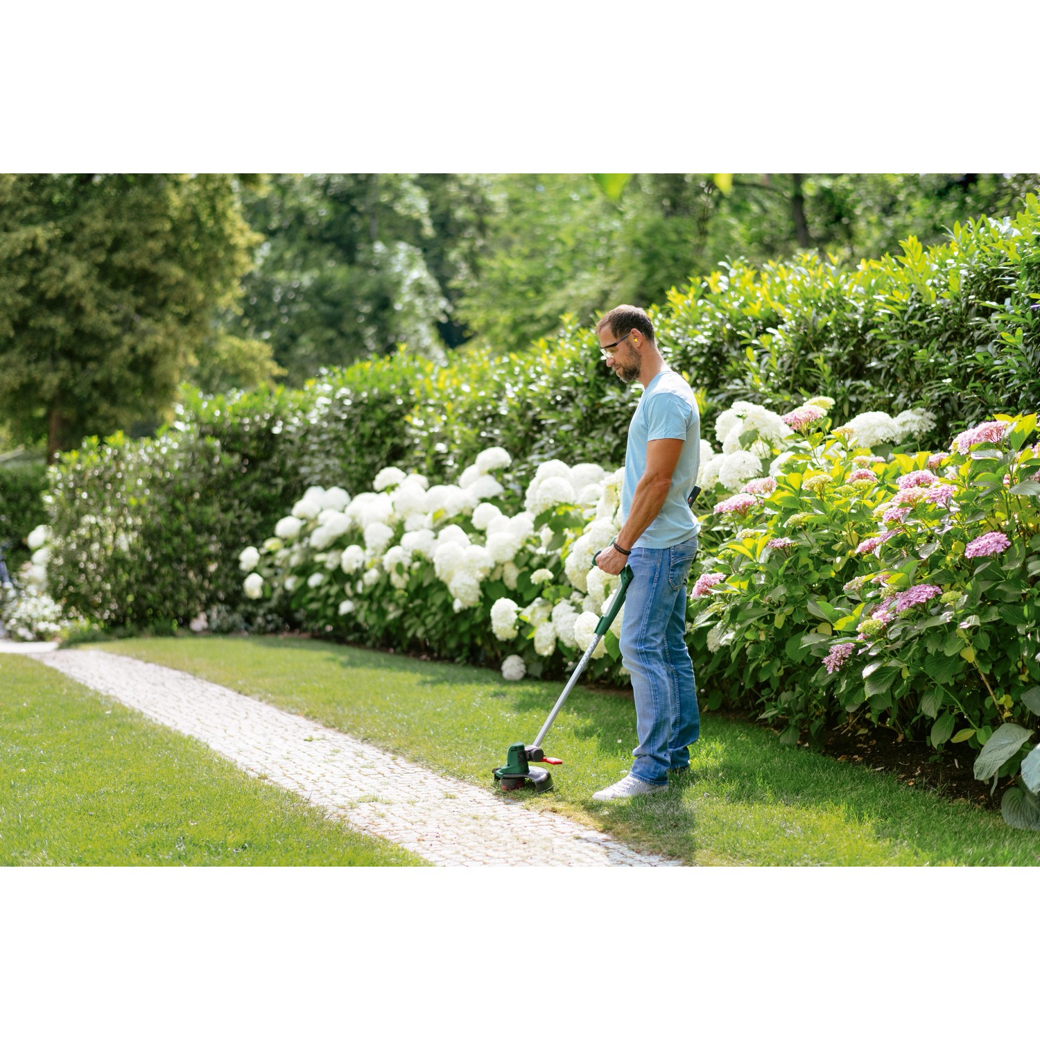 Mann benutzt Bosch Akku-Rasentrimmer UniversalGrassCut 18V-26 im Garten.