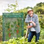 Grünes Relaxdays Tomatengewächshaus aus Stahl und PVC mit reifen Tomatenpflanzen im Garten. Ein lächelnder Gärtner.