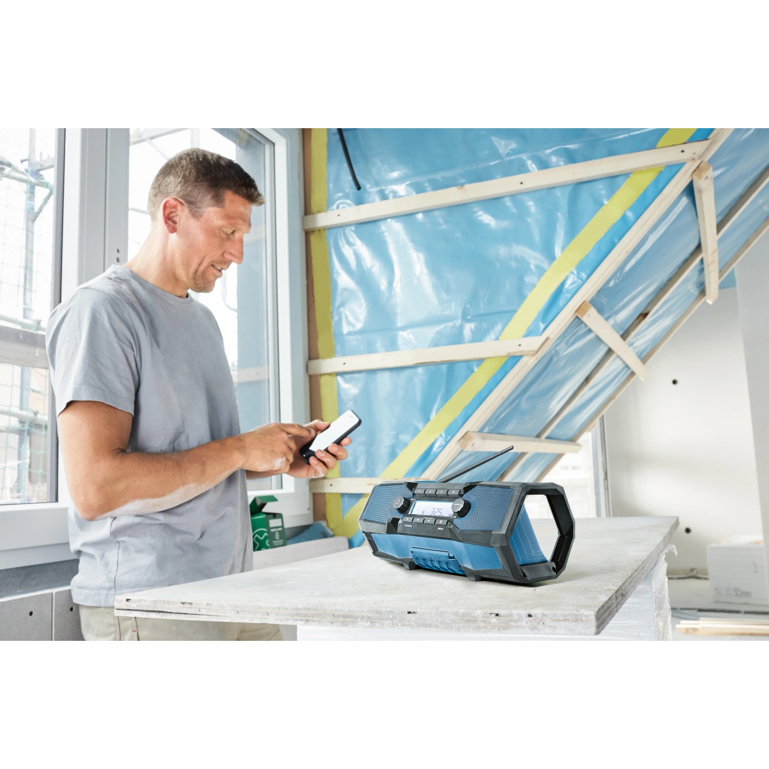 Bosch Professional Akku-Radio GPB 18V-2 C Solo mit Mann und Smartphone auf Baustelle.