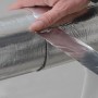 Hand klebt glänzendes Aluminium Klebeband auf eine silberne Rohrisolierung. Dämmstoffzubehör für Rohrschalen und Lamellenmatten.