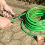 Wolfcraft Outdoormesser schneidet grünen Gartenschlauch. Messer mit Köcher für Camping & Garten.