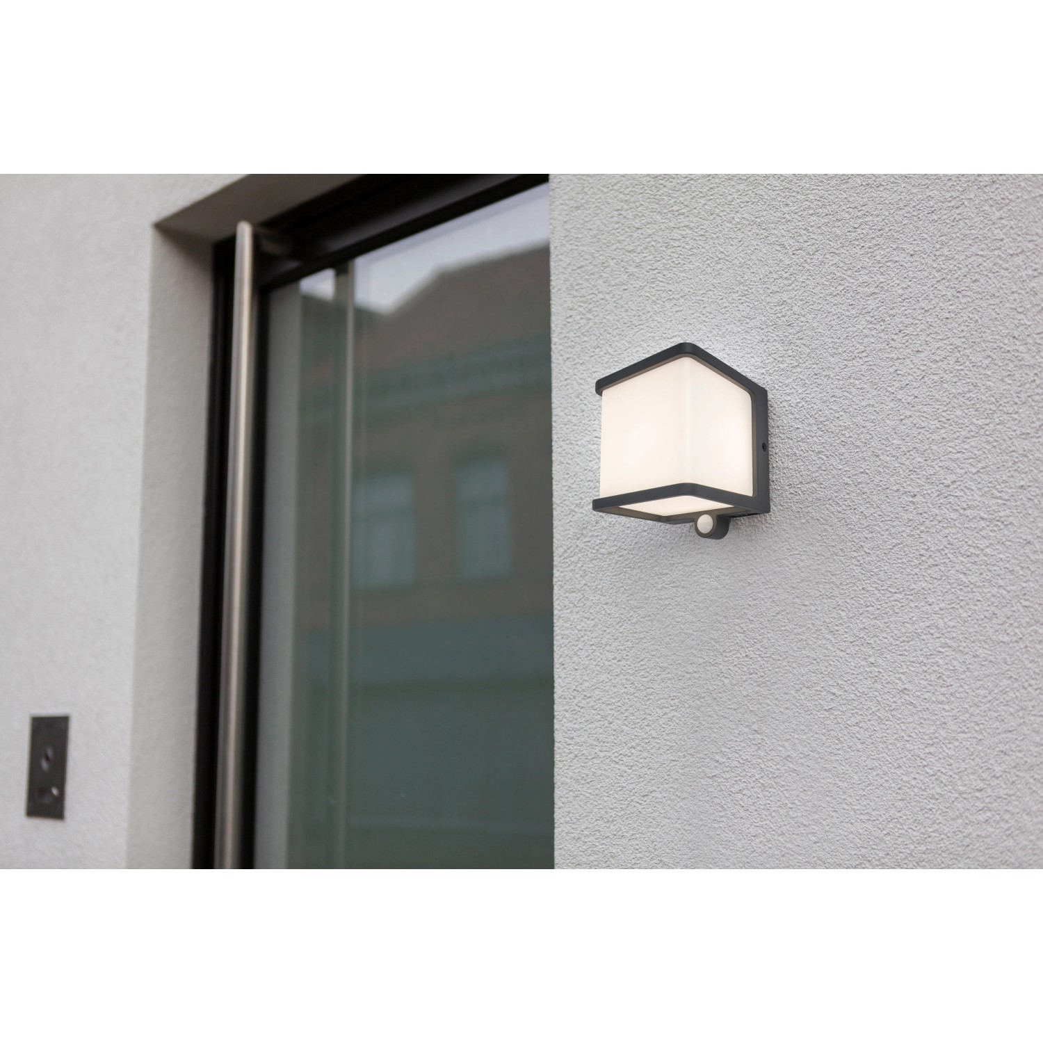 Anthrazitfarbene Lutec LED Solar Wandleuchte Doblo mit Bewegungsmelder an einer weißen Wand.