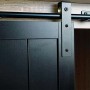 Detailaufnahme: Naturfarbener MCW Schrank K75 mit schwarzer Schiebetür und Metallschiene.
