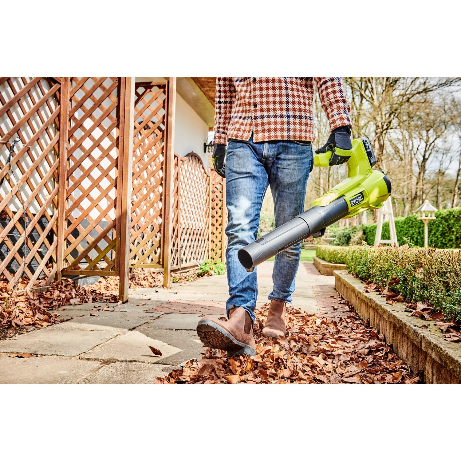 Mann nutzt Ryobi Akku-Laubgebläse RY18BLA-140 One+ zum Laub entfernen im Garten.