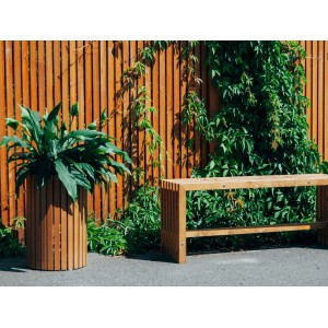 Lackierter, runder Pflanzkasten Quadra (Ø 34 cm) aus Naturholz mit grüner Pflanze im Garten.