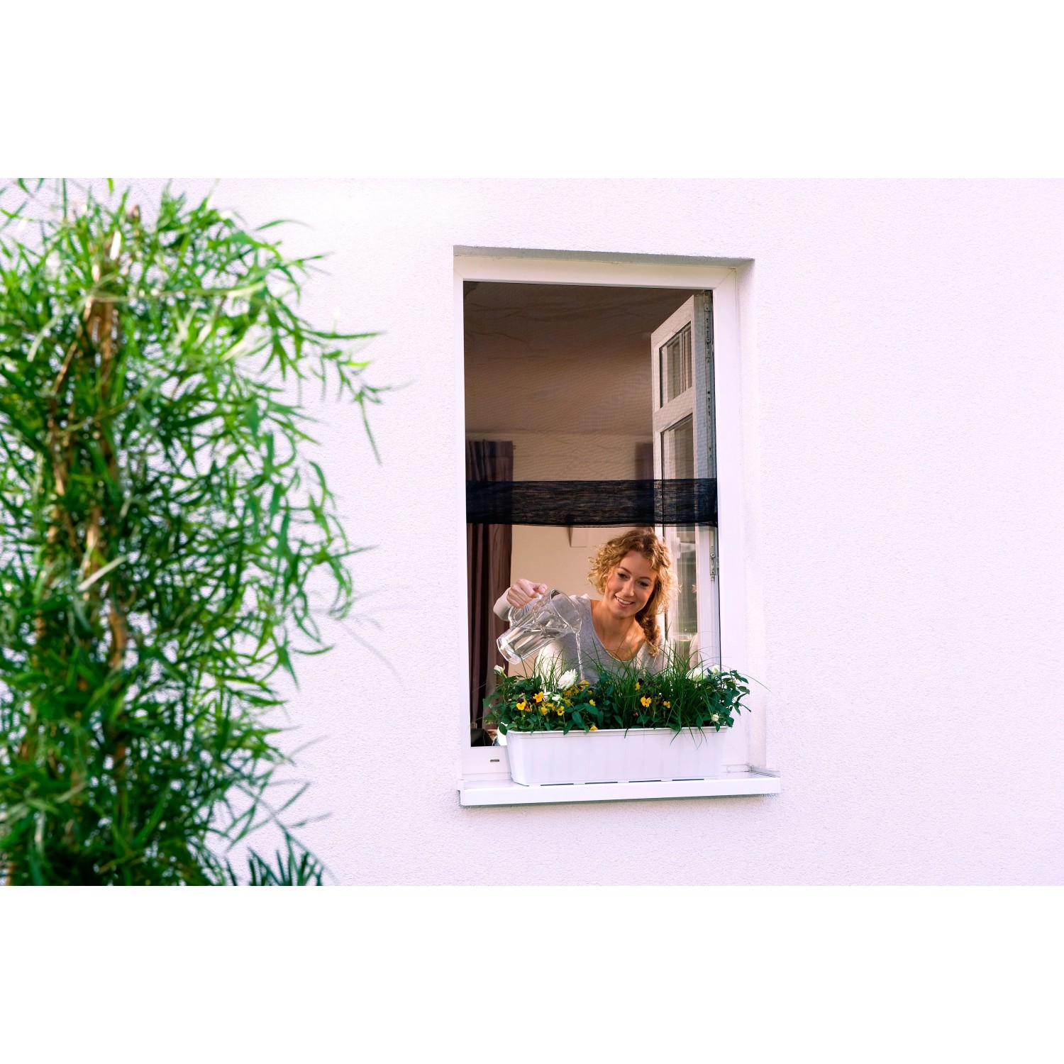 Frau gießt Blumen hinter anthrazitfarbenem tesa Fliegengitter Fenster Open/Close.