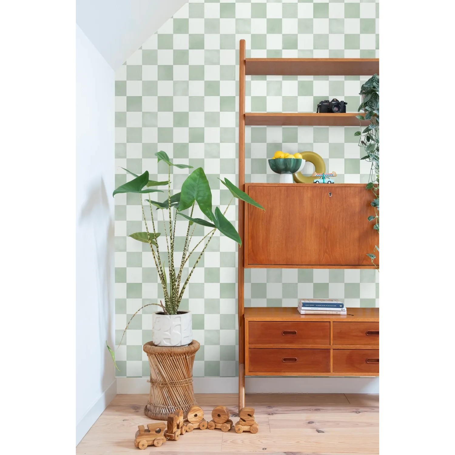 ESTAhome Vliestapete mit grün-weißem Karomuster an einer Wand, daneben Holzregal und Pflanze. Dekorative Tapete.