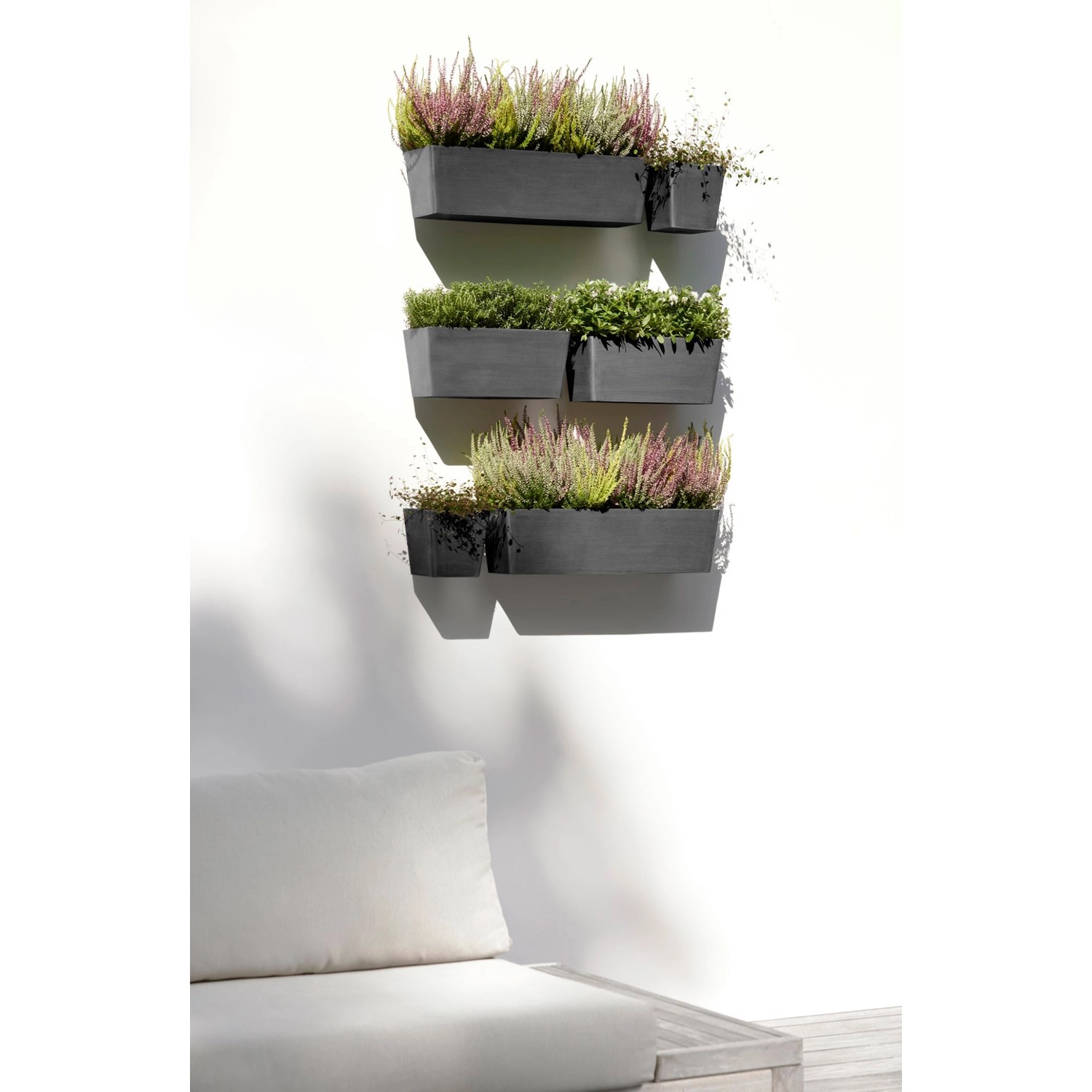Ecopots Manhattan Wall L Hängetöpfe in Dunkelgrau, bepflanzt an einer Wand.