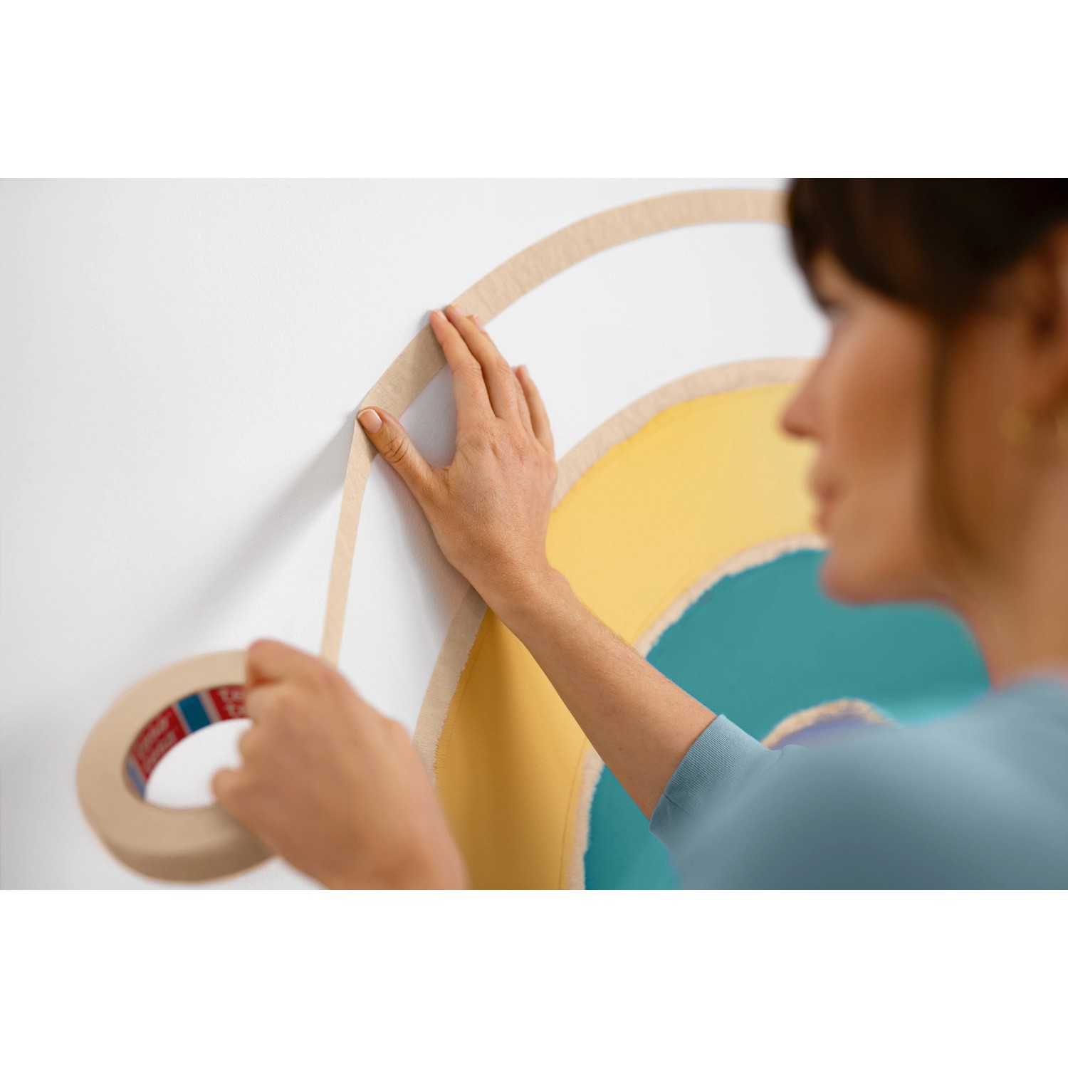 Frau klebt mit Tesa Malerband Kurven ein Wandbild ab.