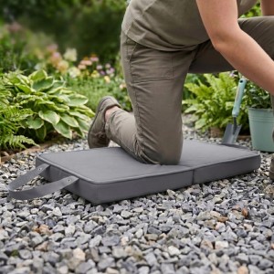 Graue, faltbare Relaxdays Garten Kniematte auf Kies. Eine Person kniet darauf beim Gärtnern. Stoßdämpfender Knieschutz.