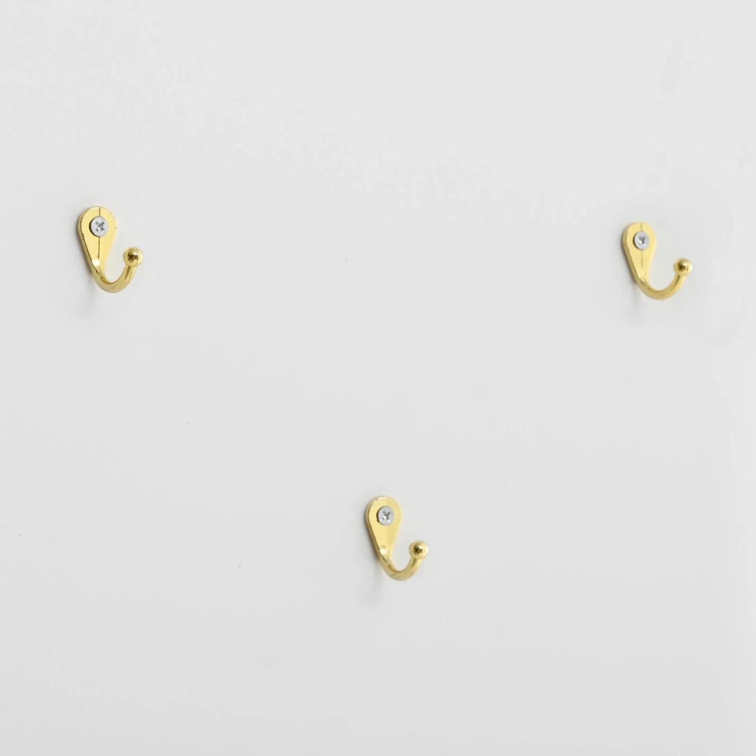 Drei goldene Haken auf weißer Oberfläche, Detail des Garderobenschranks mit Schuhkommode.
