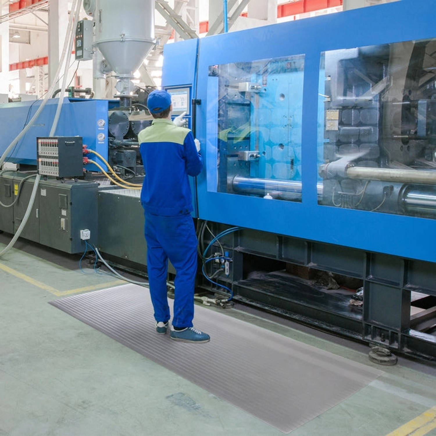 Graue KARAT Anti-Ermüdungsmatte Softer-Work-Mat unter Arbeiter an Maschine.