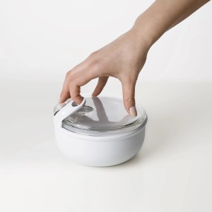 Runde, weiße Rotho Frischhaltedose Ela (0,75 l) mit transparentem Deckel wird von einer Hand verschlossen.