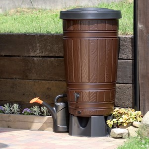 Braune Waterform Regentonne Woodcan 265 l in Holzoptik mit Gießkanne im Garten.
