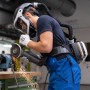Person mit schwarzem Dräger X-plore 8500 Atemschutzhelm und Gebläseeinheit schleift Metall. Schutz vor Partikeln.