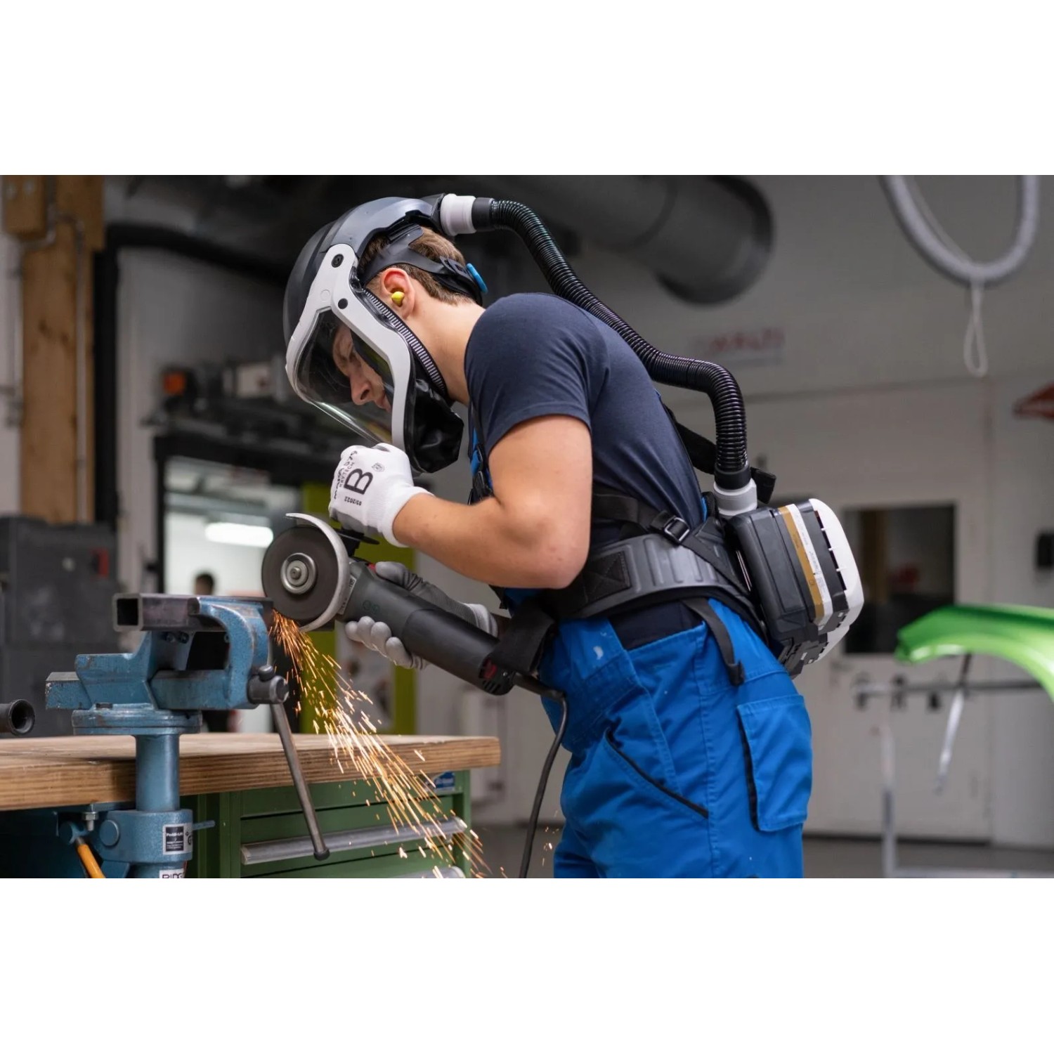 Person mit schwarzem Dräger X-plore 8500 Atemschutzhelm und Gebläseeinheit schleift Metall. Schutz vor Partikeln.