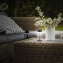 Brilo Akku-LED-Tischleuchte Kira, anthrazit, Ø 8 cm, 19 cm hoch, auf Gartentisch mit Deko.