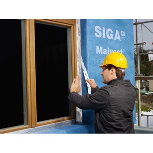 Handwerker verarbeitet Siga Majvest Fassadenbahn am Fenster. Dämmstoffzubehör für winddichte Gebäudehülle.