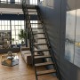Minka Raumspartreppe Flex Hybrid: Schwarze Metalltreppe mit Eiche-Stufen im modernen Innenbereich. Ideal für Galerien.