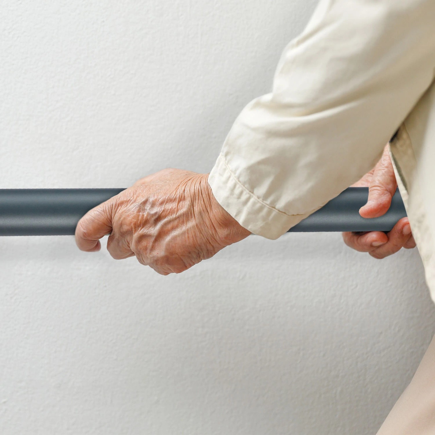 Hände einer älteren Person greifen einen anthrazitfarbenen Aluminium Handlauf an einer Wand für sicheren Halt beim Treppensteigen.