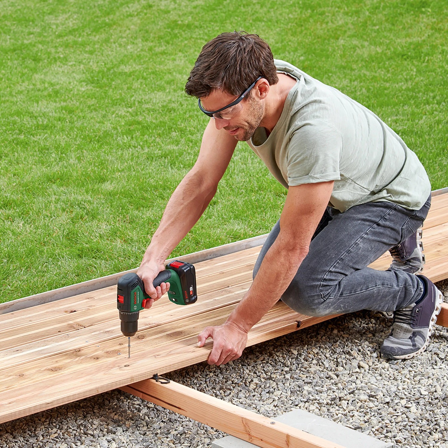 Mann schraubt mit Bosch 18V Akku-Bohrschrauber UniversalDrill 18V-60 ein Brett fest.
