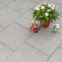 Verlegte, graue Gehwegplatten 30x30 mit Fase, dekoriert mit Pflanze, Figur und Laterne.