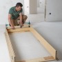 Mann montiert Türfutter mit Wolfcraft Türfutterstrebe Easy. Spannwerkzeug zur Montage von Türrahmen.