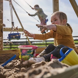 Kind spielt im WICKEY Sandkasten King Kong mit Deckel, mit Schaufel und Eimer im Sand.