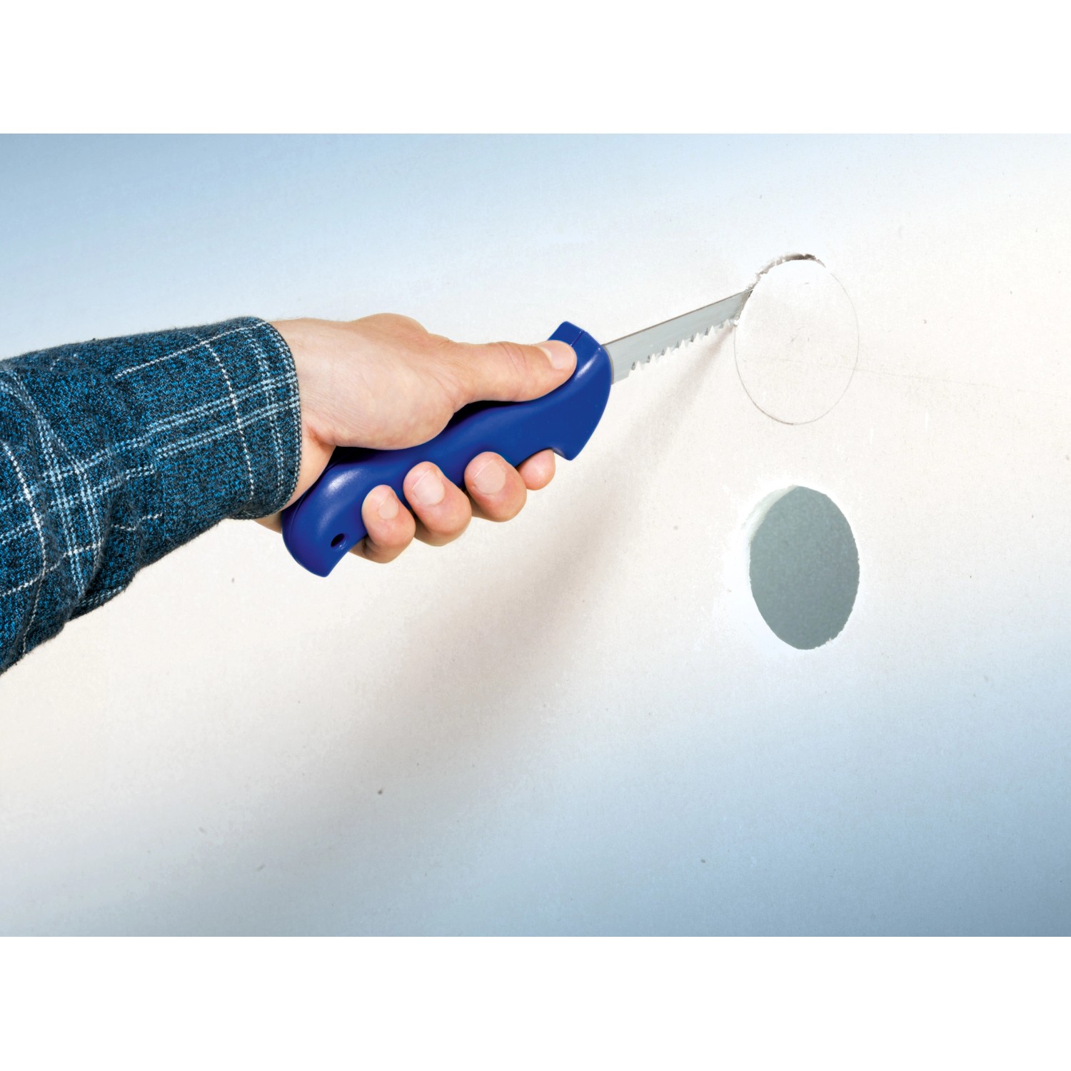 Hand schneidet mit LUX Gipskartonsäge Classic ein Loch in eine weiße Gipskartonwand.