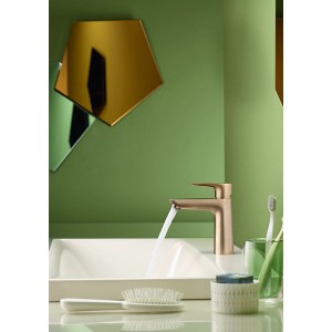 Hansgrohe Talis E Waschtischarmatur 110 in Bronze mit Wasserlauf vor grünem Hintergrund.