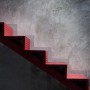 Schwarze LED Solar-Wandleuchte Pacita über roter Treppe an grauer Wand.