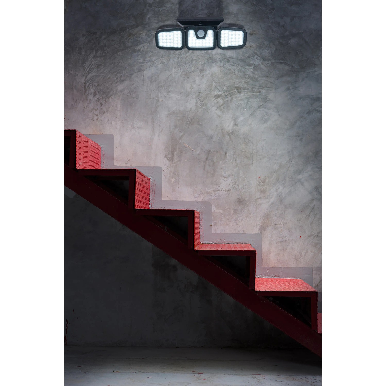 Schwarze LED Solar-Wandleuchte Pacita über roter Treppe an grauer Wand.