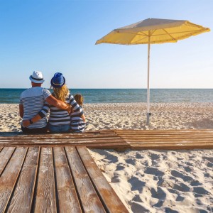 Familie entspannt am Strand unter einem gelben Sonnenschirm, sicher befestigt mit einem Rasendorn. Ideal für Garten & Camping.