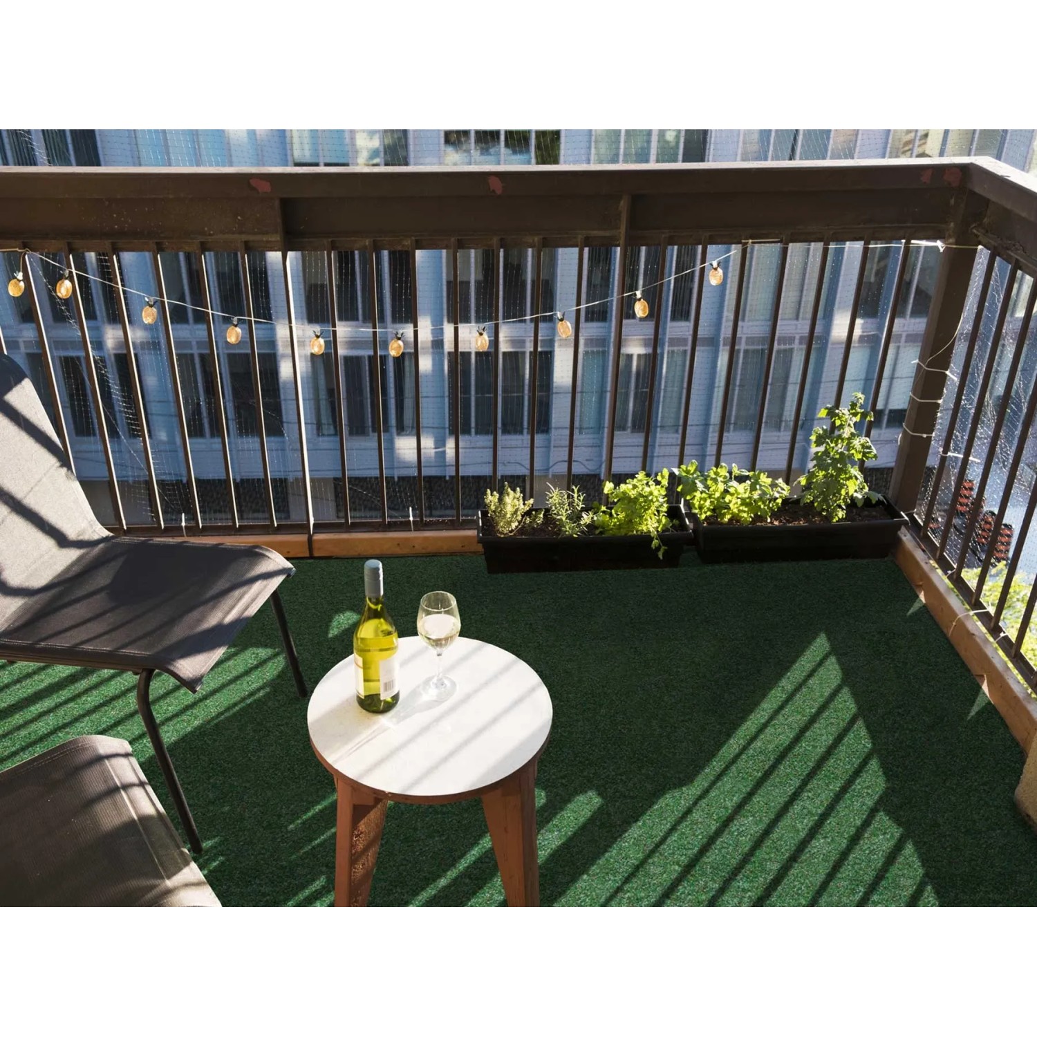 Balkon mit grünem Primaflor Rasenteppich, Tisch mit Wein und Lichterkette.