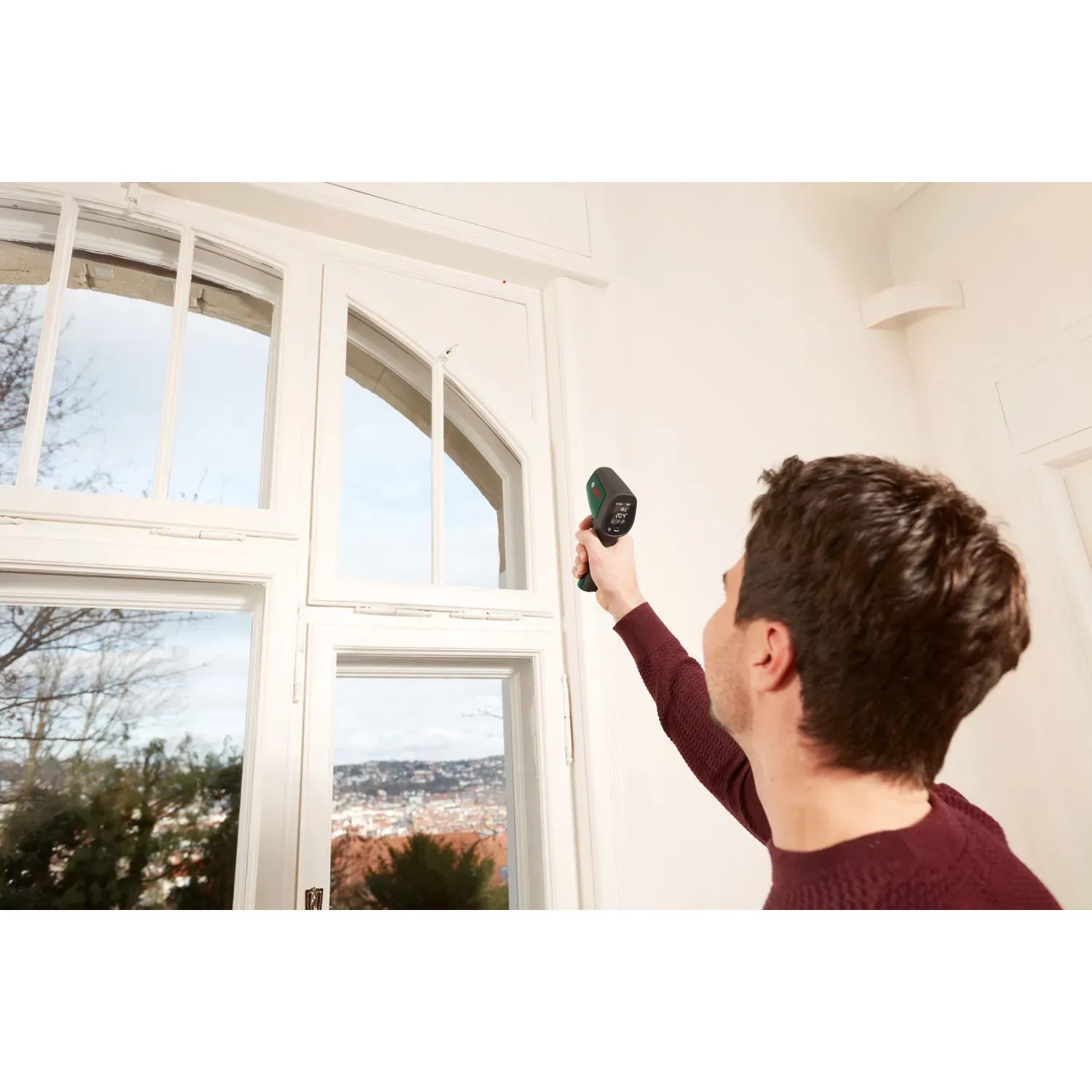 Mann misst mit Bosch UniversalTemp Infrarot-Thermometer Temperatur eines Fensters.