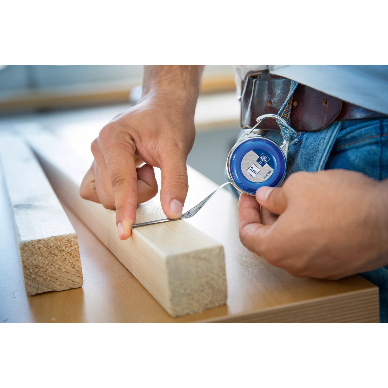 LUX Mini-Maßband 2 m im Einsatz: Hand misst Holz mit blauem Rollbandmaß.