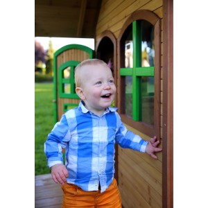 Lachender Junge vor dem braun-grünen Axi Alex Spielhaus aus Holz mit Veranda.