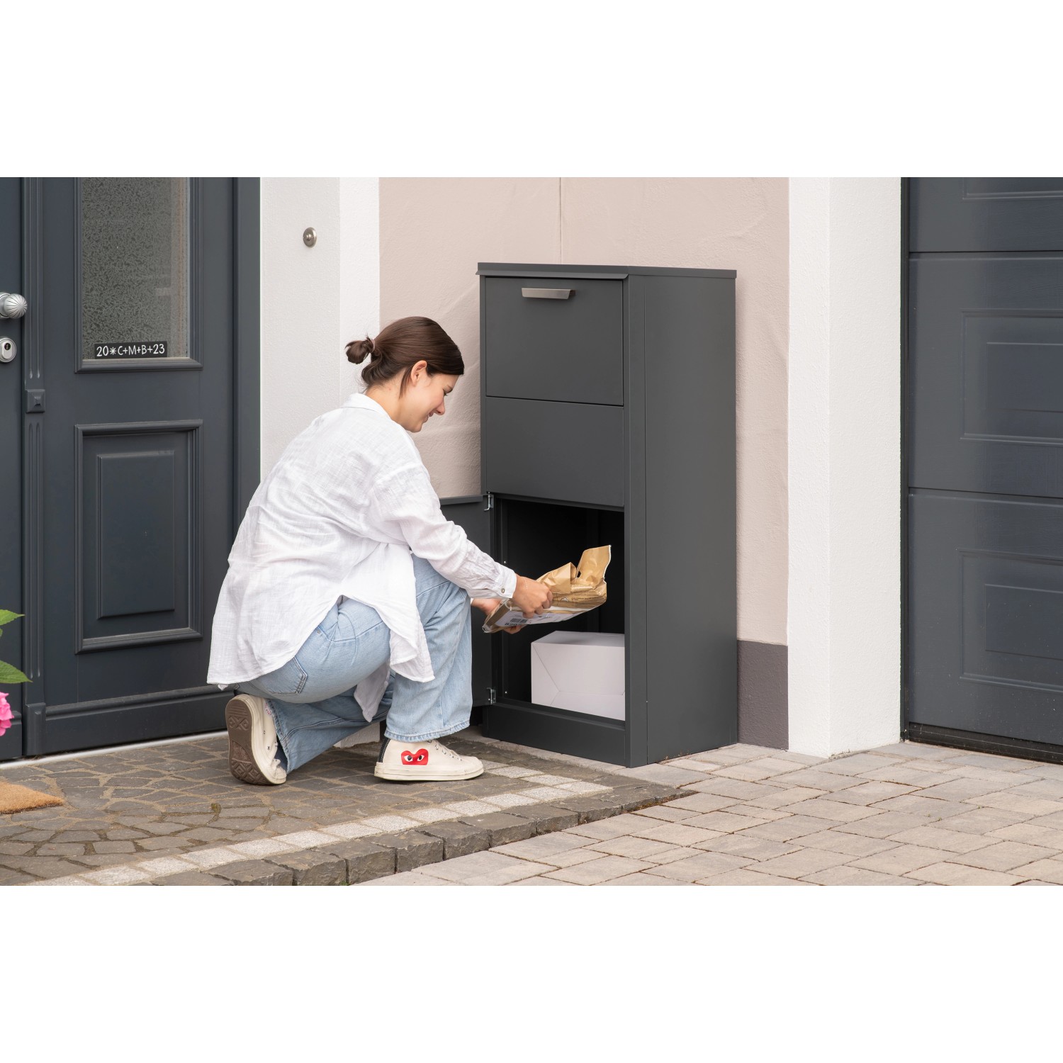 Westmann Paketbox Pepe Anthrazit: Frau entnimmt Paket aus abschließbarem Fach des Stahl-Briefkastens.