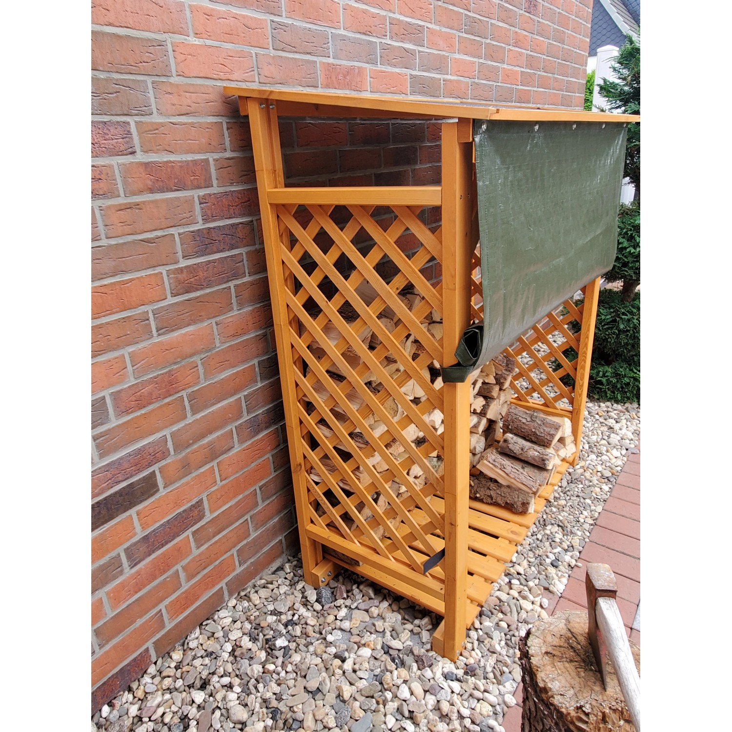 Honigbraunes Kaminholzregal Speyer mit Wetterschutzplane an einer Backsteinmauer.