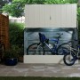 Geöffnete, hellbeige Duramax Fahrradbox mit Fahrrädern im Garten.