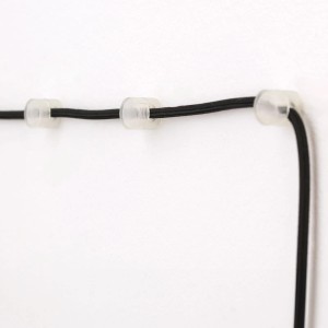 Transparente Orion Lightstyle Kabelhalter aus Kunststoff mit schwarzem Kabel an einer weißen Wand.
